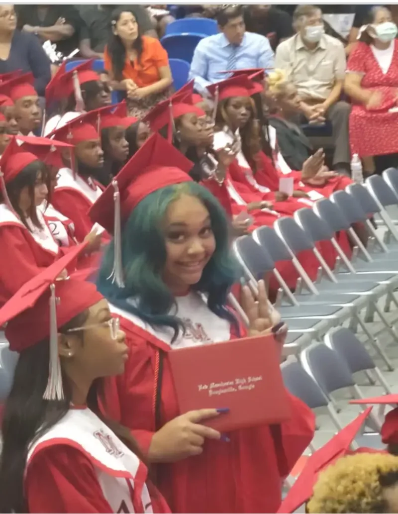 A graduate in a red cap and gown holding her diploma at commencement