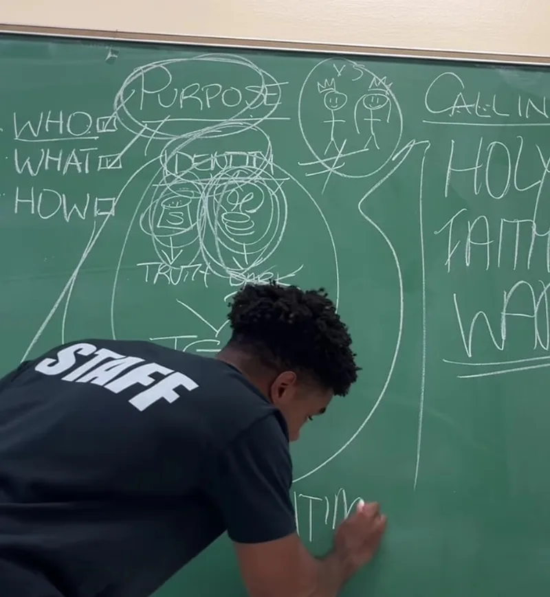 A staff member writing a lesson on a classroom chalkboard